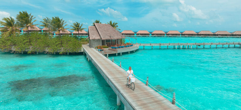 Overwater villas in the Maldives with a person cycling on a boardwalk.